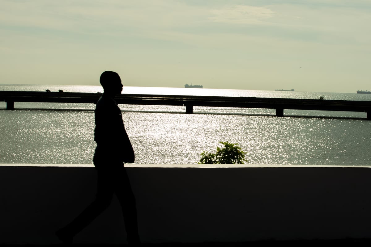 Silhouette of a man walking past the shimmering sea at golden hour